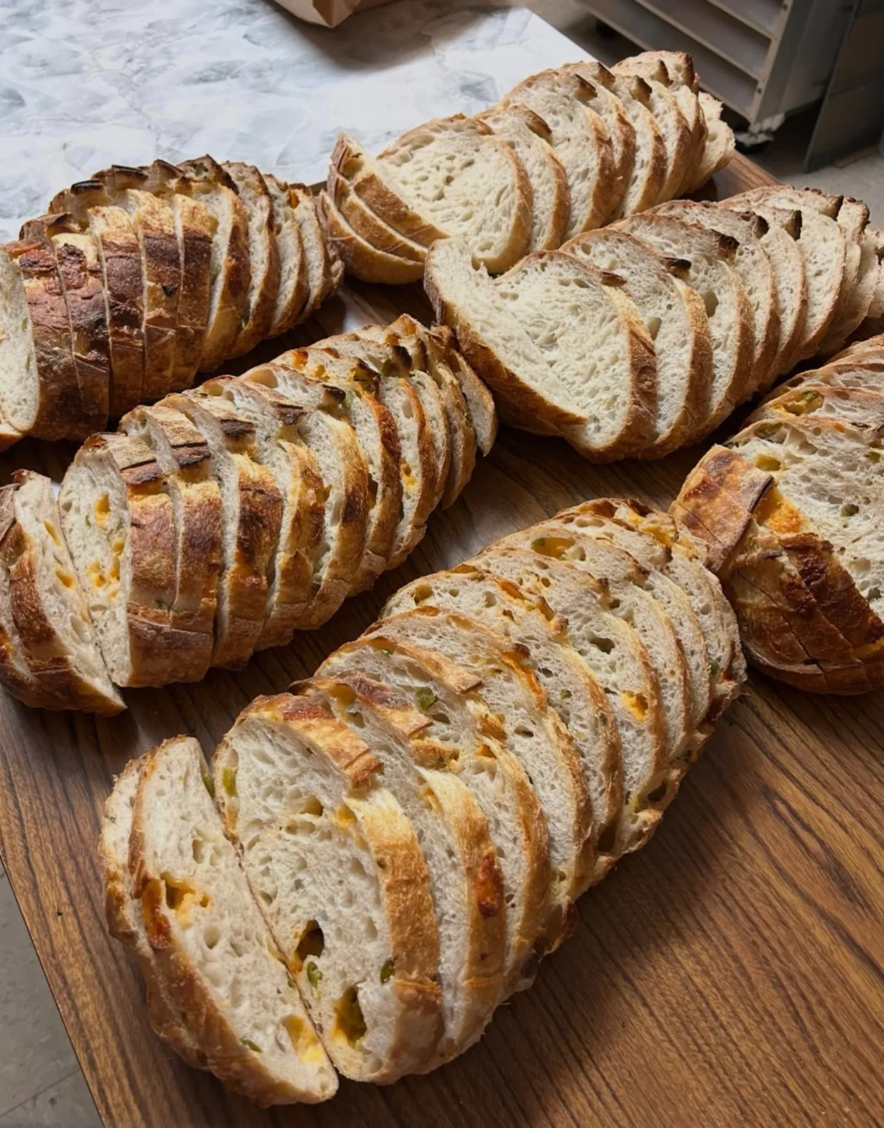 Loaves of sourdough sliced on a wooden table, some with jalapeño and cheddar